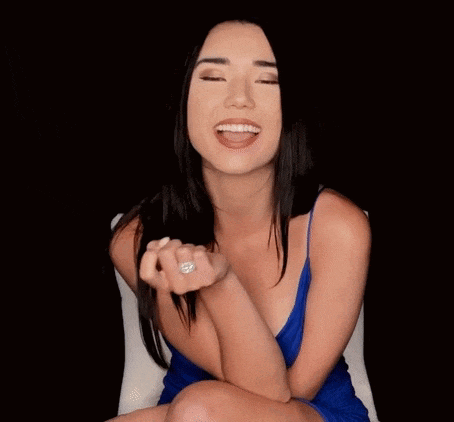 a woman in a blue dress is sitting in a chair and smiling while making an ok sign .