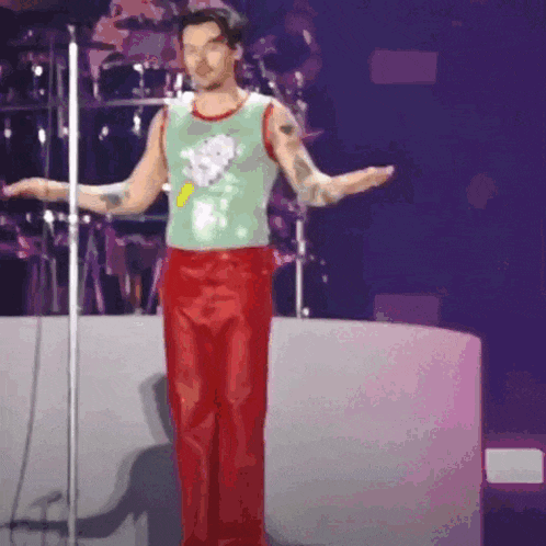 a man in a green tank top and red pants is standing in front of a microphone .