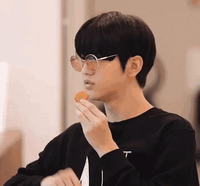 a young man wearing sunglasses and a black shirt is eating a chicken nugget .