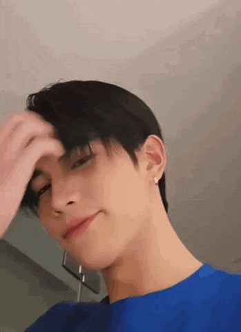 a young man in a blue shirt is touching his hair while smiling .