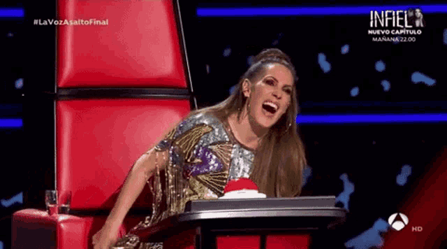 a woman is sitting in a red chair laughing while holding a red button .