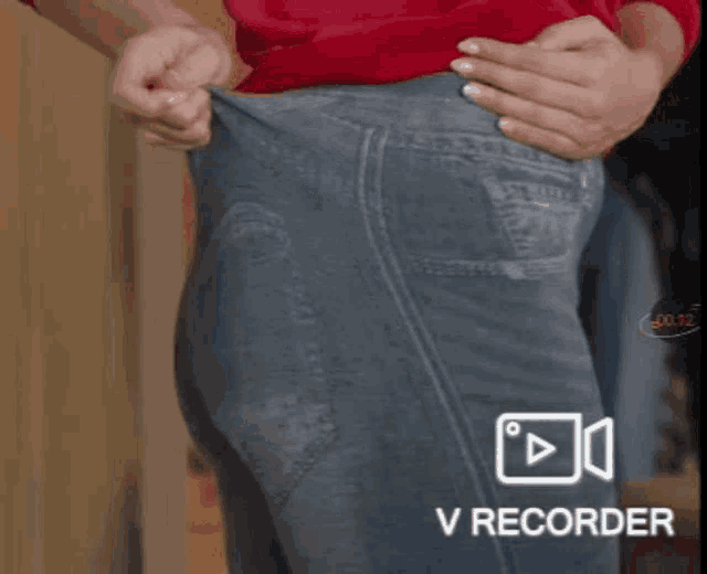 a person wearing a red shirt and blue jeans is pulling up their pants .