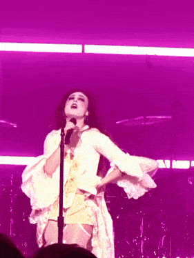 a woman in a white dress singing into a microphone on a stage