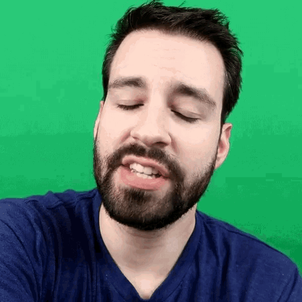 a man with a beard and a blue shirt is making a funny face with his eyes closed .