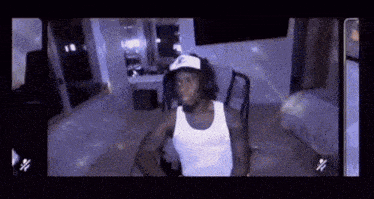 a man in a white tank top is sitting in a chair in a room .
