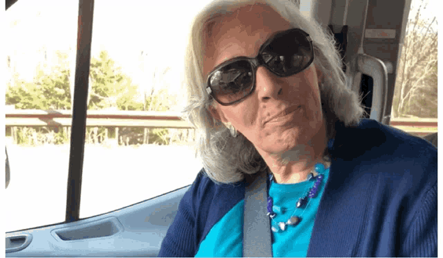 an elderly woman wearing sunglasses and a blue shirt is sitting in a car