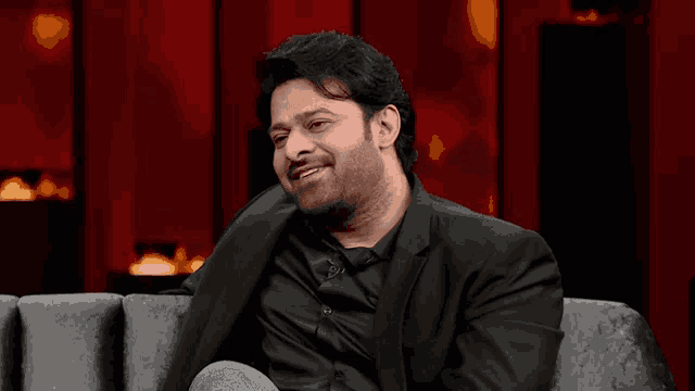 a man in a suit is sitting on a couch and smiling