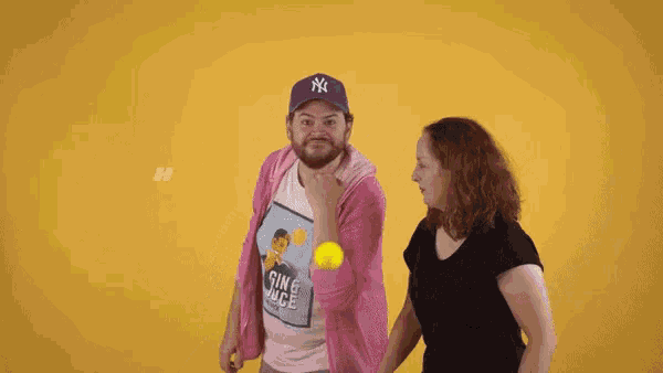 a man wearing a ny hat holds a tennis ball next to a woman wearing a shirt that says sing & dance