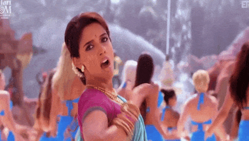 a woman in a pink top is standing in front of a crowd of women in bikinis .