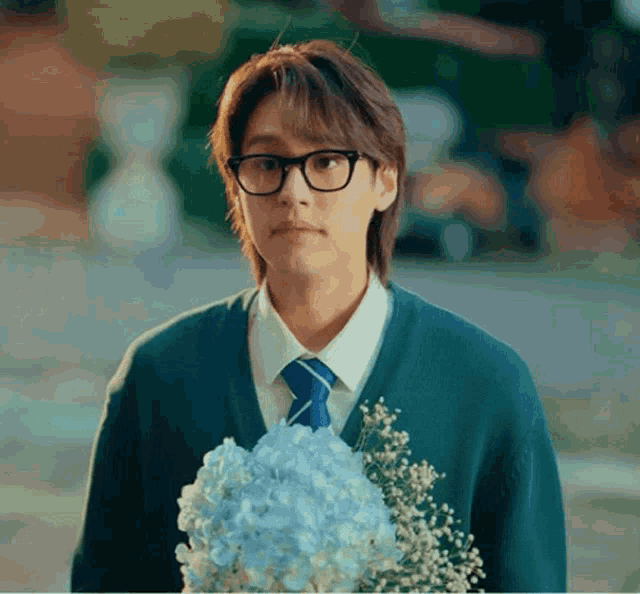 a young man wearing glasses holds a bouquet of flowers