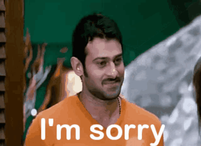 a man in an orange shirt says i 'm sorry in white letters