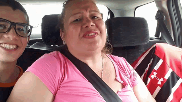 a woman in a pink under armour shirt sits next to a boy in a car