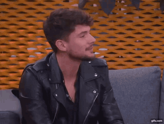 a man in a leather jacket is sitting on a couch