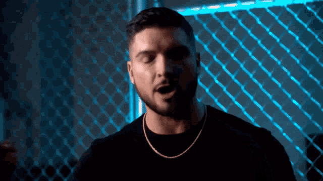 a man with a beard is singing in front of a chain link fence in a dark room .