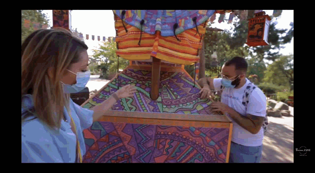 a man and a woman wearing face masks are looking at a colorful painting