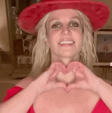 britney spears is wearing a red cowboy hat and making a heart shape with her hands .
