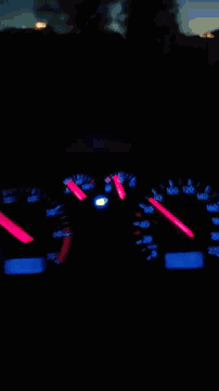 a blurred image of a car 's dashboard at night with a red and blue speedometer