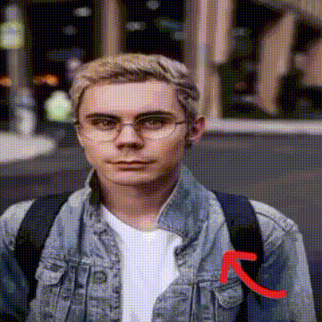 a young man wearing glasses and a denim jacket is standing on a city street .
