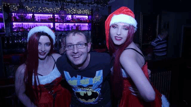a man is posing for a picture with two women in santa hats in a bar .