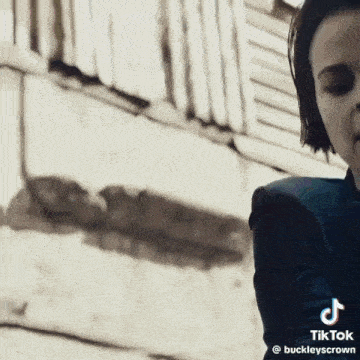 a woman in a suit is smoking a cigarette in front of a wall .