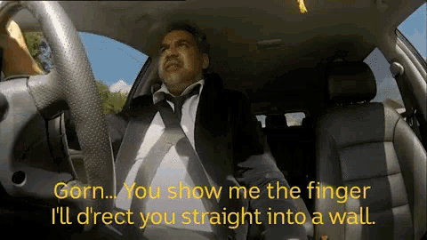 a man in a suit and tie is driving a car and saying gorn