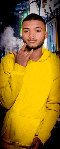 a young man wearing a yellow hoodie stands in front of a building with the letter m on it