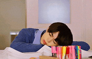 a young man is sleeping on a pile of papers next to a stack of markers .