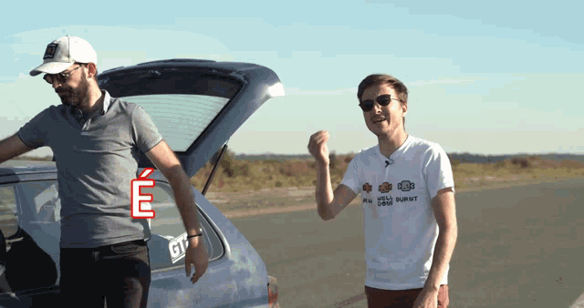 two men are standing next to a car with the trunk open and one of them is wearing a t-shirt that says e