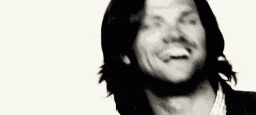 a black and white photo of a man with long hair and a beard smiling with his mouth open .
