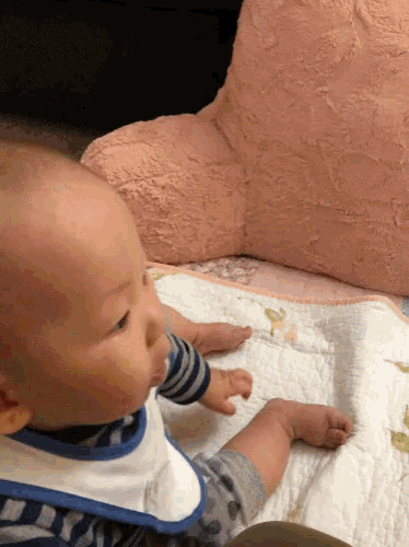 a baby wearing a bib and striped shirt is sitting on a bed