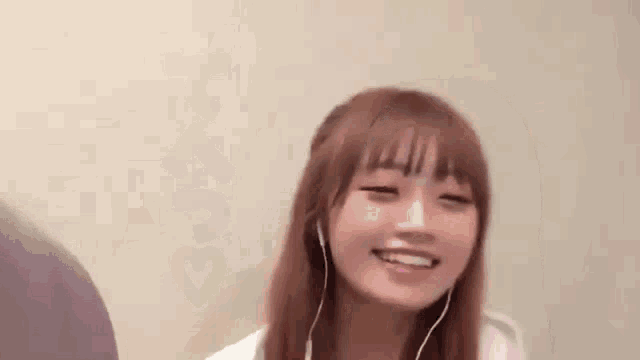 a young woman wearing headphones is smiling while sitting in front of a wall .