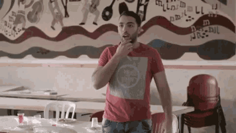 a man in a red shirt is standing in a room with a mural on the wall behind him .