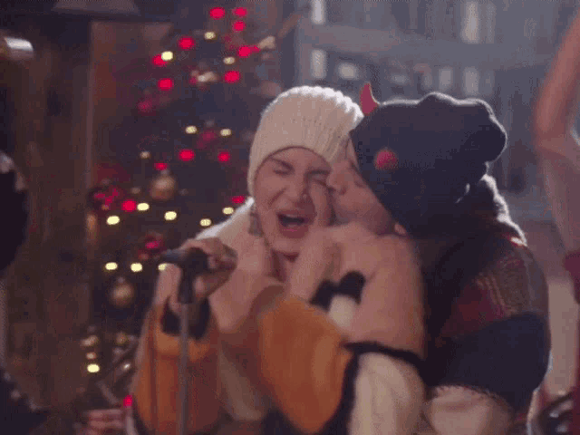 a man in a beanie kisses a woman on the cheek in front of a microphone