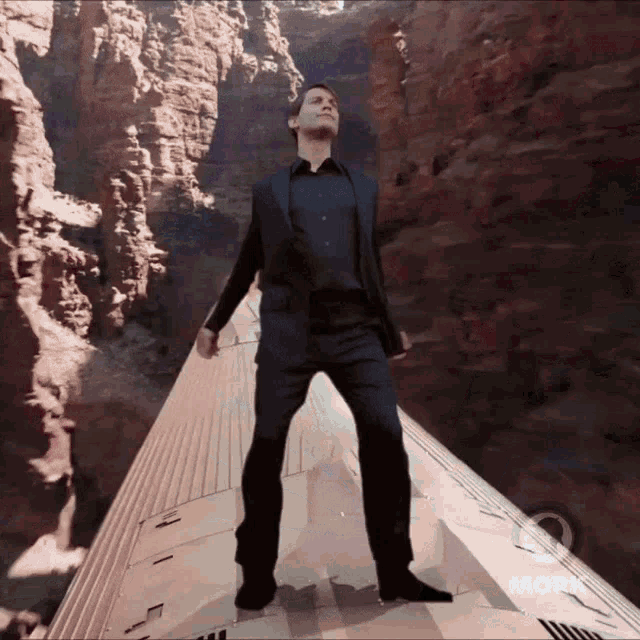 a man in a suit is standing on the side of a train with a canyon in the background