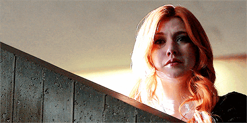 a woman with red hair is standing in front of a concrete wall