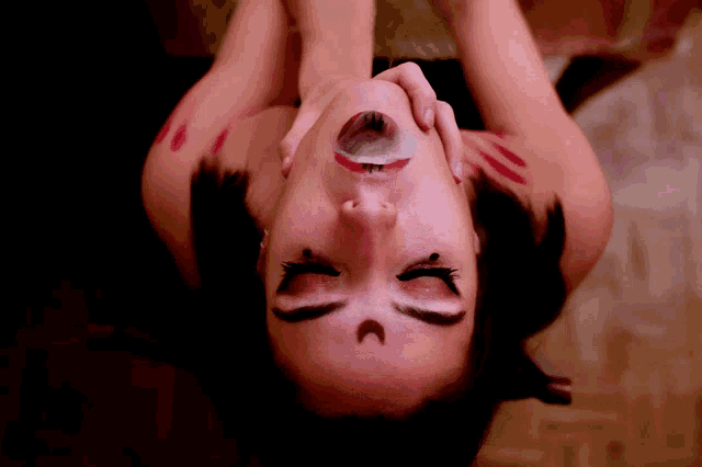 a woman with a crescent moon tattoo on her face is laying down with her mouth open