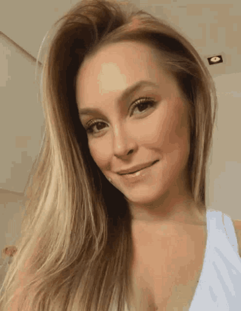 a woman with long blonde hair wearing a white tank top