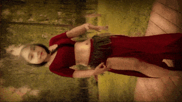 a woman in a red dress is standing on a wooden deck with trees in the background