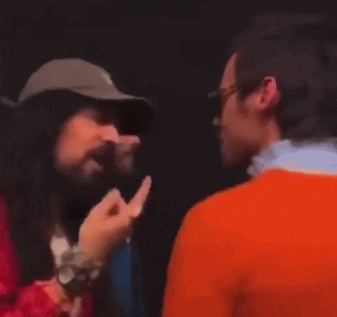 a man with a beard is giving a middle finger to another man in an orange shirt .