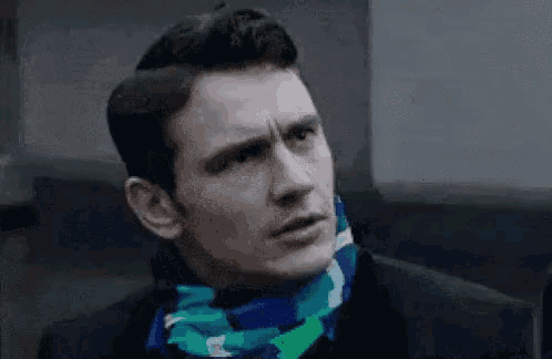 a man wearing a black suit and a blue scarf around his neck is making a funny face .