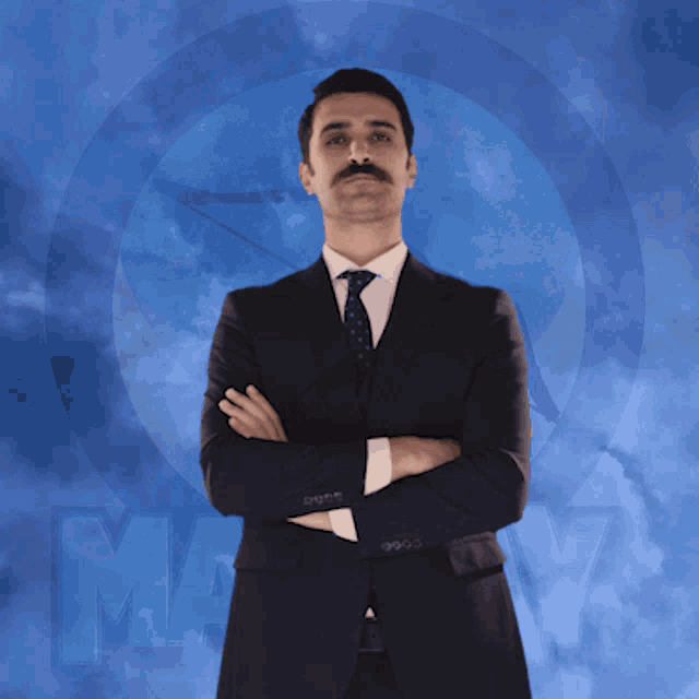 a man in a suit and tie stands with his arms crossed in front of a blue background that says may