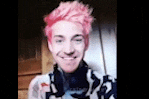 a man with pink hair is smiling for the camera .