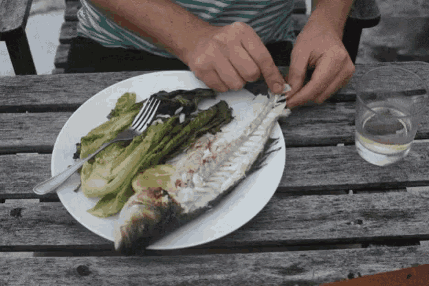 a person is taking a piece of fish from a white plate