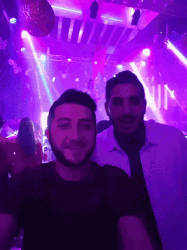 two men are posing for a picture in a club with purple lights and the word nun on the wall