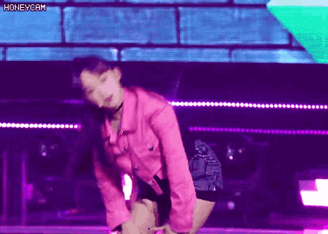 a woman in a pink jacket is dancing on a stage with purple lights .