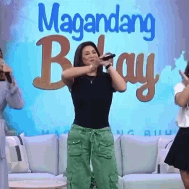 a woman is singing into a microphone in front of a sign that says magandang bayay