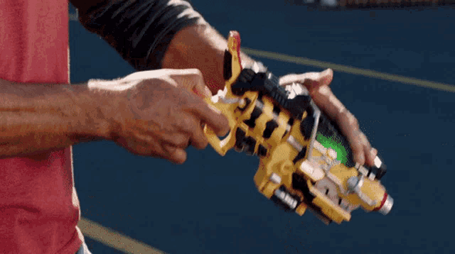 a man in a red shirt is holding a yellow and black toy dinosaur