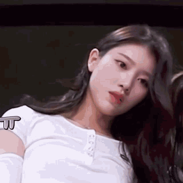 a close up of a woman with long hair wearing a white shirt and looking at the camera .
