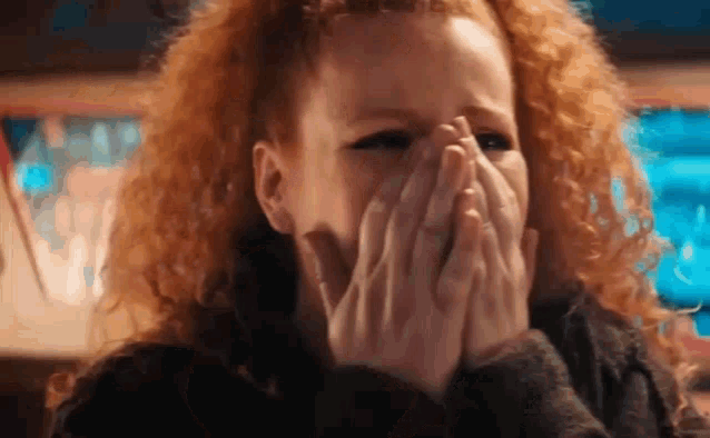 a woman with curly red hair is covering her mouth with her hands .