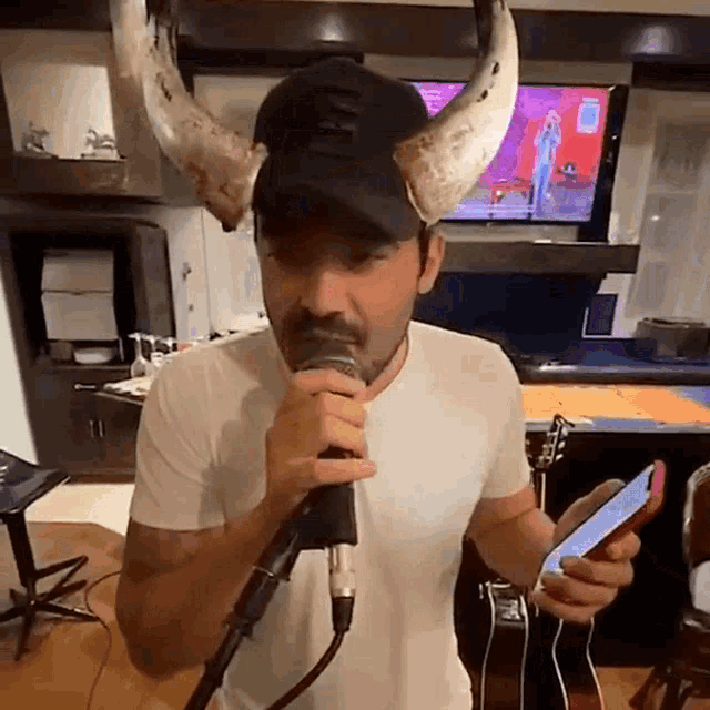 a man wearing a horned hat is singing into a microphone and holding a cell phone